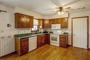 Une cuisine avec des meubles de rangement en bois, un four à micro-ondes, une cuisinière et un ventilateur de plafond.