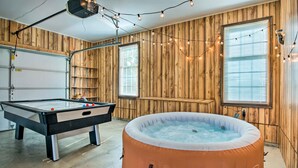 Une pièce avec une table de billard, un jacuzzi gonflable de marque Coleman, des murs en bois et des guirlandes lumineuses.