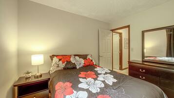 Une chambre à coucher avec un lit, une table de chevet, une commode, un miroir et une porte.