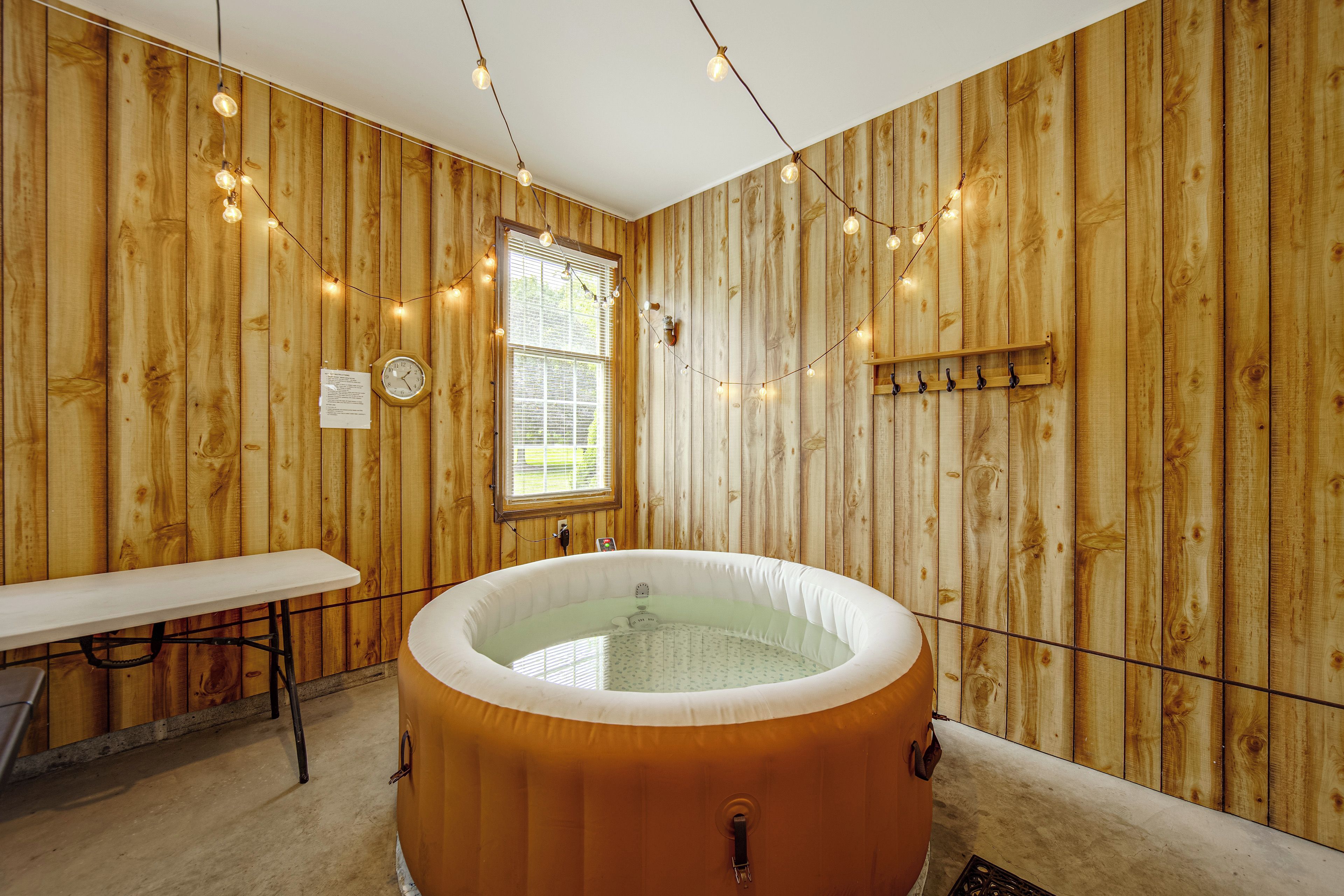 A wooden room with a hot tub, a table, and a window with blinds.