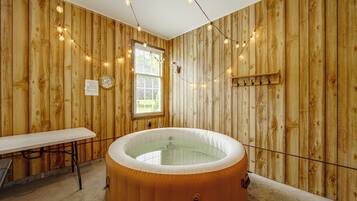 A wooden room with a hot tub, a table, and a window with blinds.