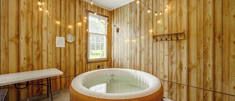 A wooden room with a hot tub, a table, and a window with blinds.