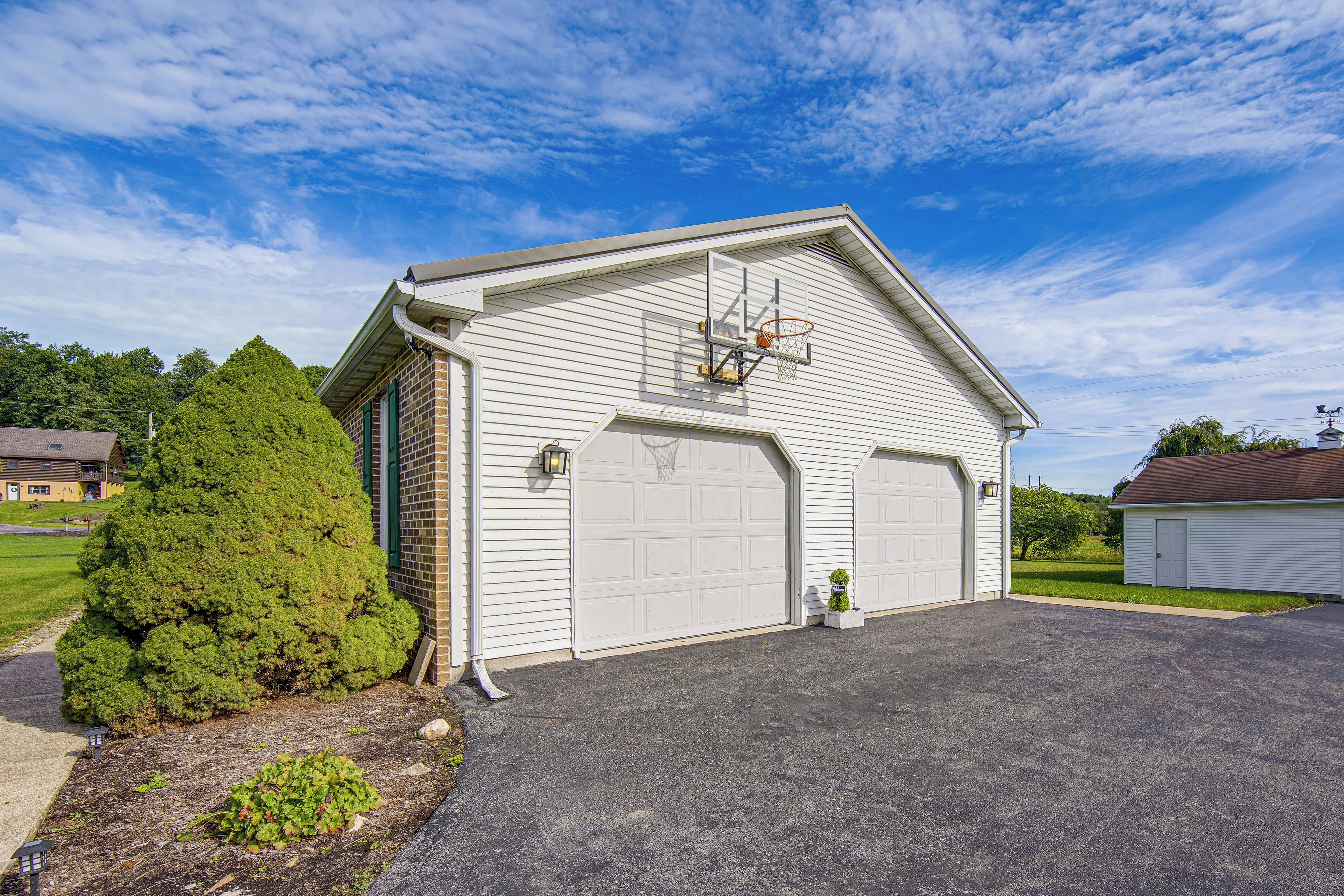 A single-story building with a garage door, a basketball hoop, and a small tree in front.