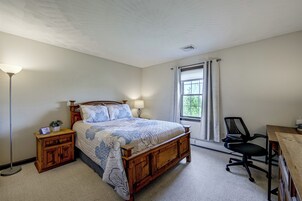 Quarto com cama, mesas de cabeceira, escrivaninha e uma cadeira.