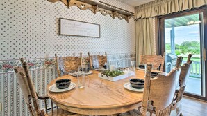 Un coin repas avec une table ronde en bois, six chaises en bois, un papier peint à motifs floraux et un panneau accroché au mur.