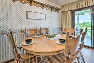 Uma sala de jantar com uma mesa redonda de madeira, seis cadeiras de madeira, papel de parede com padrão floral e uma placa na parede.