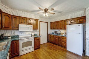 A kitchen with wooden cabinets, a white refrigerator, a stove, and a ceiling fan. - Charming Lewisburg Home w/ Hot Tub & Games! (Lewisburg)