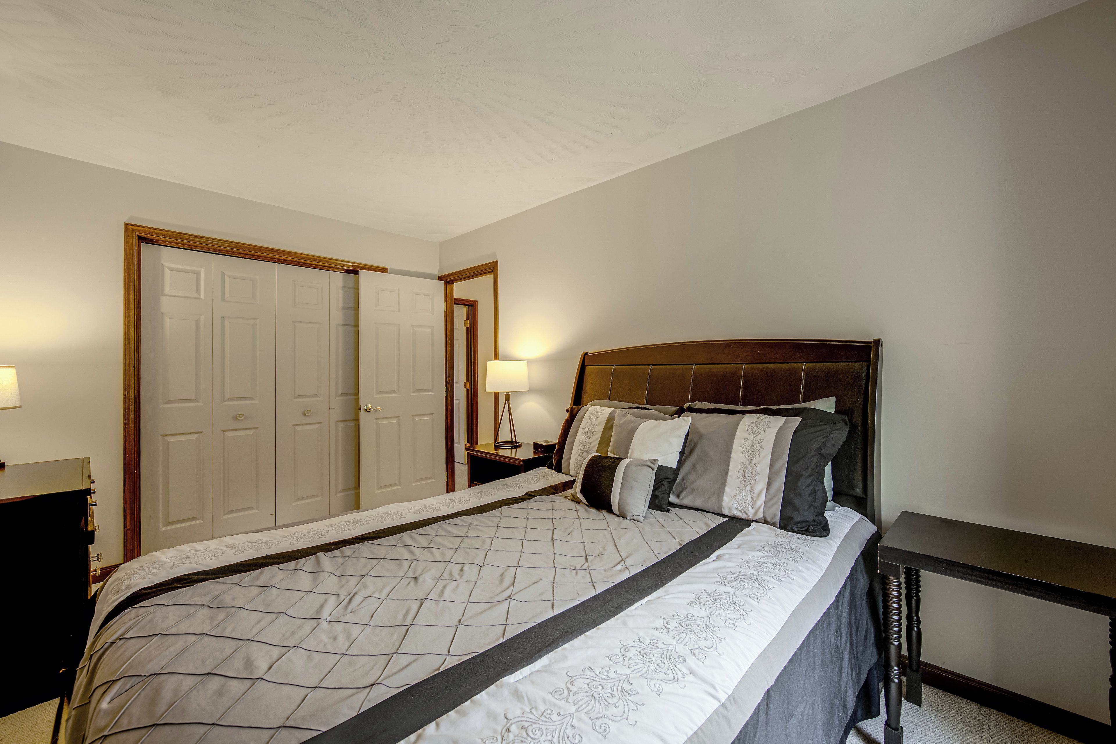 A bedroom with a large bed, a nightstand, a dresser, and a door.