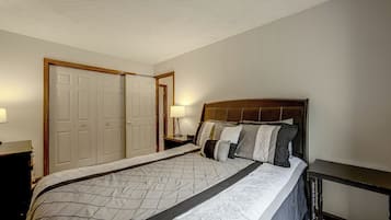 A bedroom with a large bed, a nightstand, a dresser, and a door.