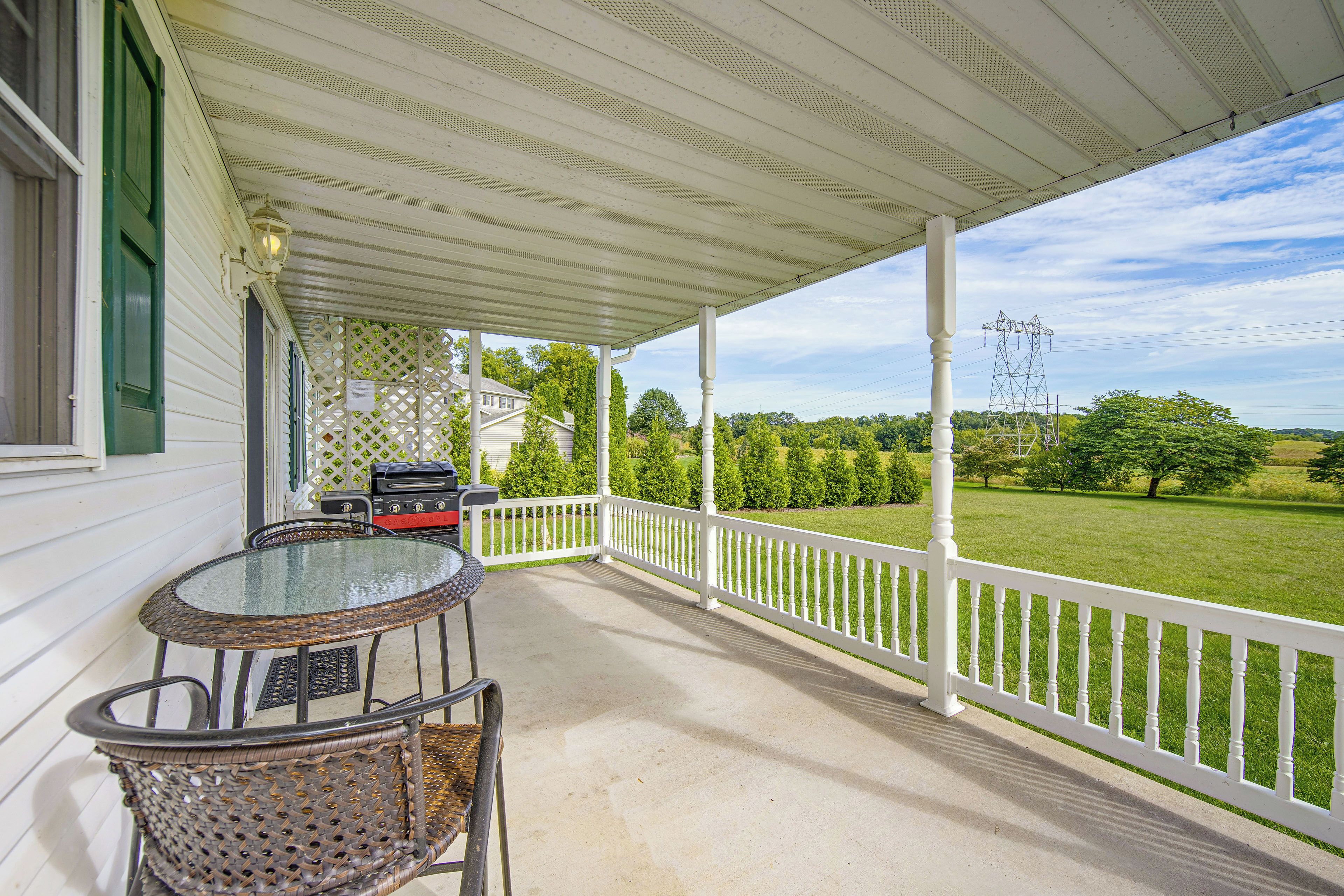 A covered porch with a table and chairs, a grill, and a view of a green landscape.