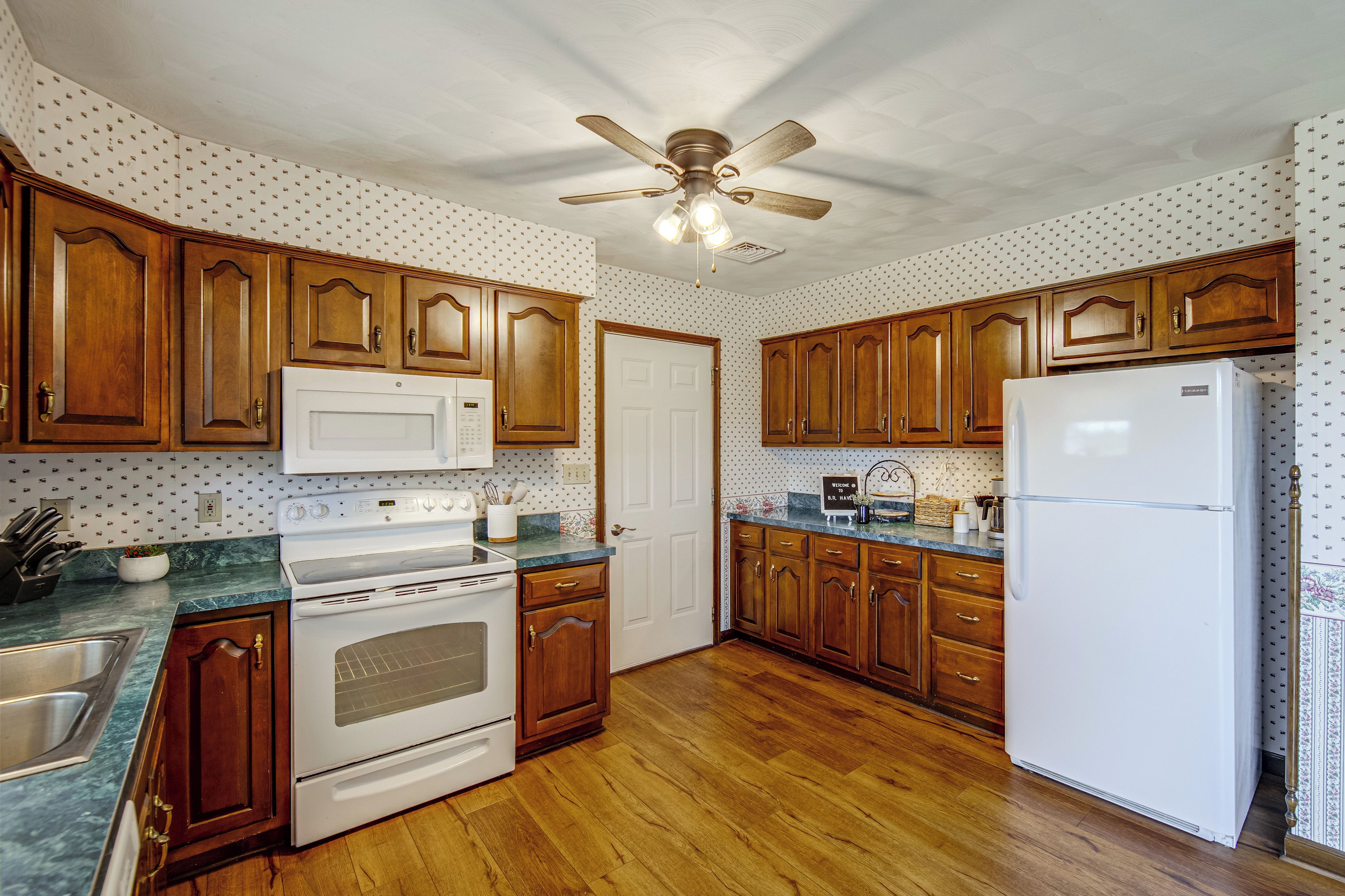 A kitchen with wooden cabinets, a white refrigerator, a stove, and a ceiling fan.