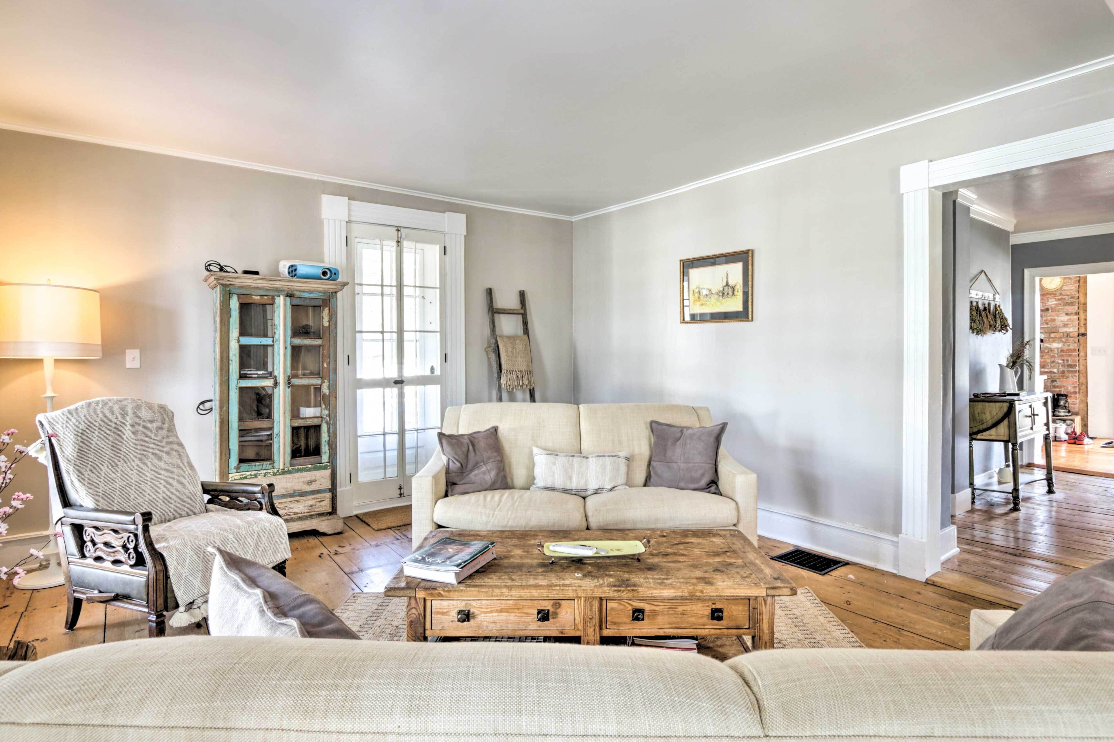 A living room with a sofa, armchair, and coffee table. There is a cabinet with glass doors and a ladder leaning against the wall.