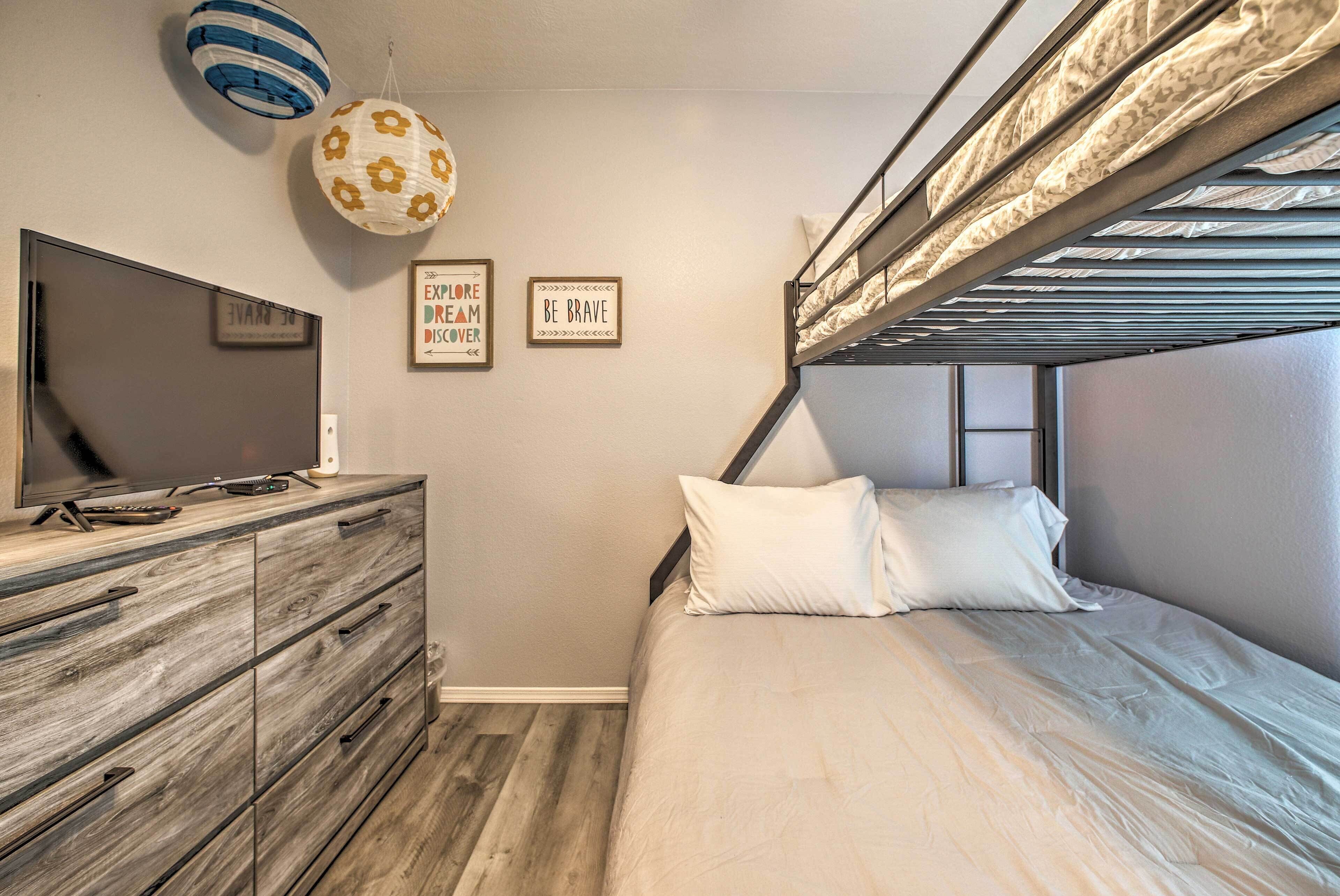 Un dormitorio con literas, un televisor sobre un aparador de madera, y decoración inspiradora en la pared.