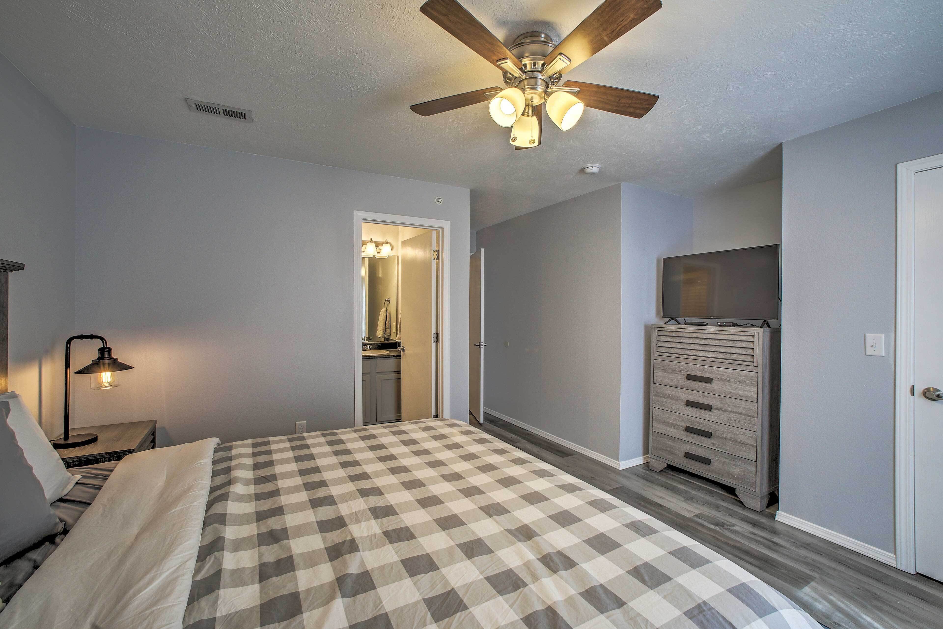 A bedroom with a bed, a ceiling fan, a dresser, and a nightstand with a lamp.