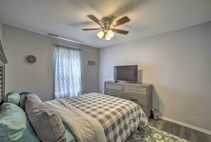 Une chambre à coucher comprenant un lit, une commode, un ventilateur de plafond, une horloge et une fenêtre avec des rideaux.