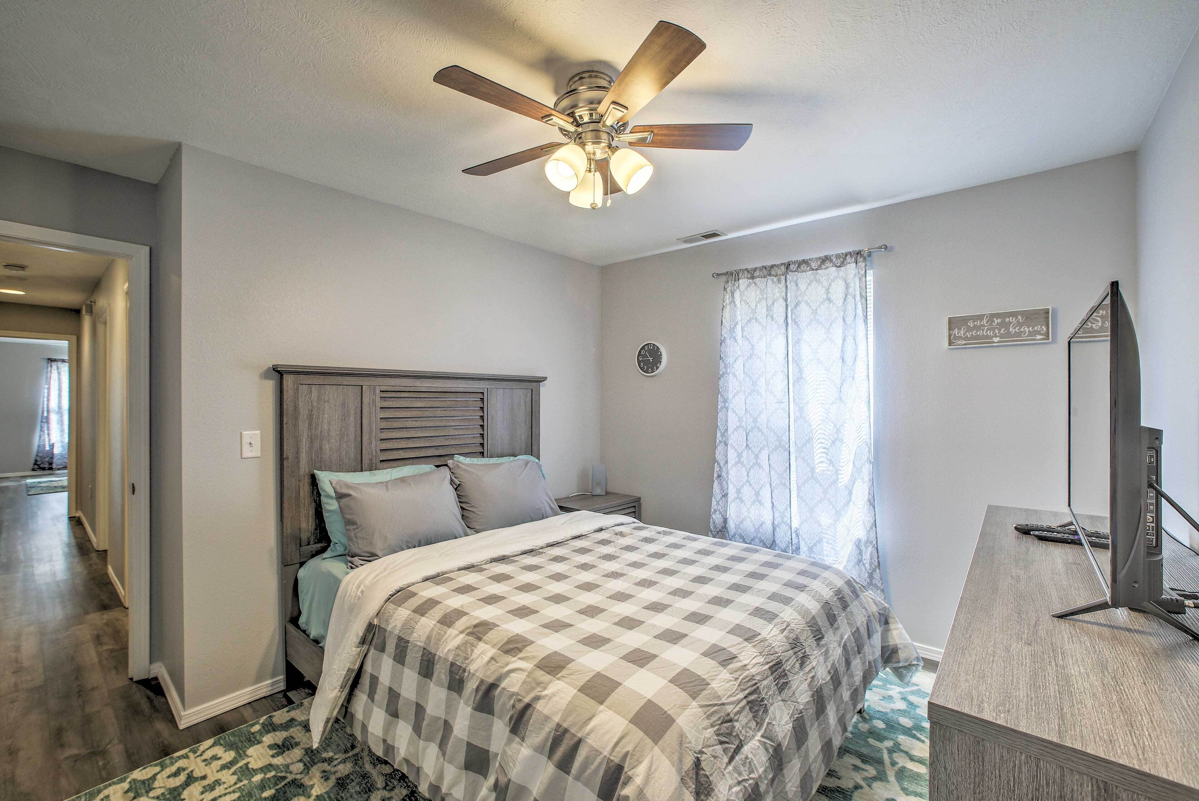 Une chambre à coucher comprenant un lit, un bureau, un ventilateur de plafond, une horloge et une fenêtre avec des rideaux.