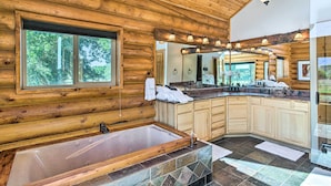 A log cabin bathroom with a large bathtub, wooden walls, a window with a view of trees, and a vanity with a mirror and lights. - 'ali River Farms' Breathtaking Mt Backdrop! (Clifton)