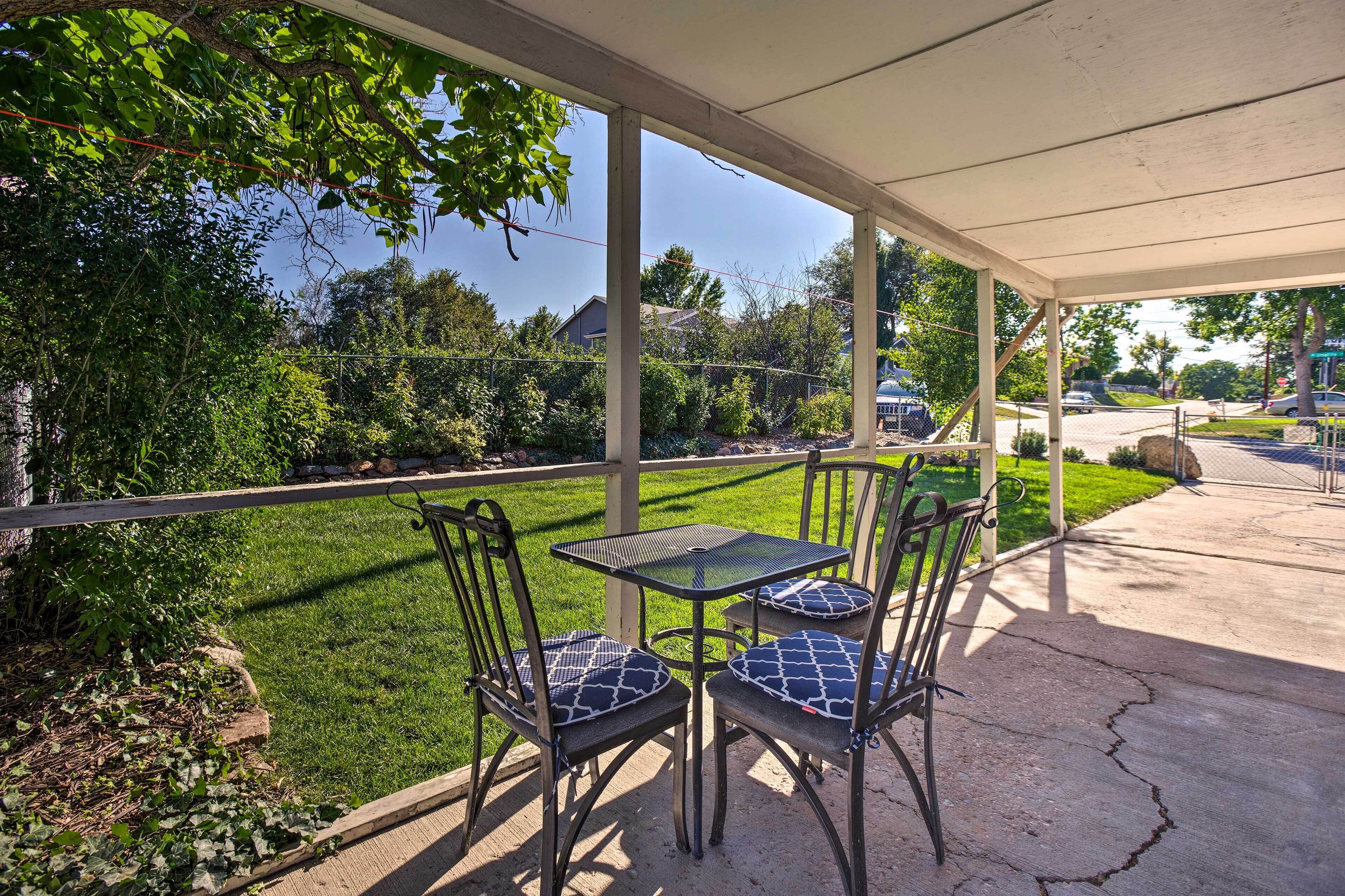 An outdoor patio with a covered seating area, including a table and chairs, overlooking a well-maintained lawn and a street view.