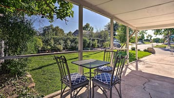 An outdoor patio with a covered seating area, including a table and chairs, overlooking a well-maintained lawn and a street view.