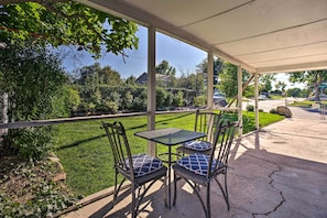 An outdoor patio with a covered seating area, including a table and chairs, overlooking a well-maintained lawn and a street view. - 4 Mi to Coors Field: Charming Apartment w/ Patio (Denver)