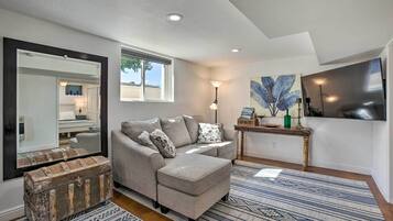 A living room with a sofa, a coffee table, a mirror, a window, and a painting on the wall.