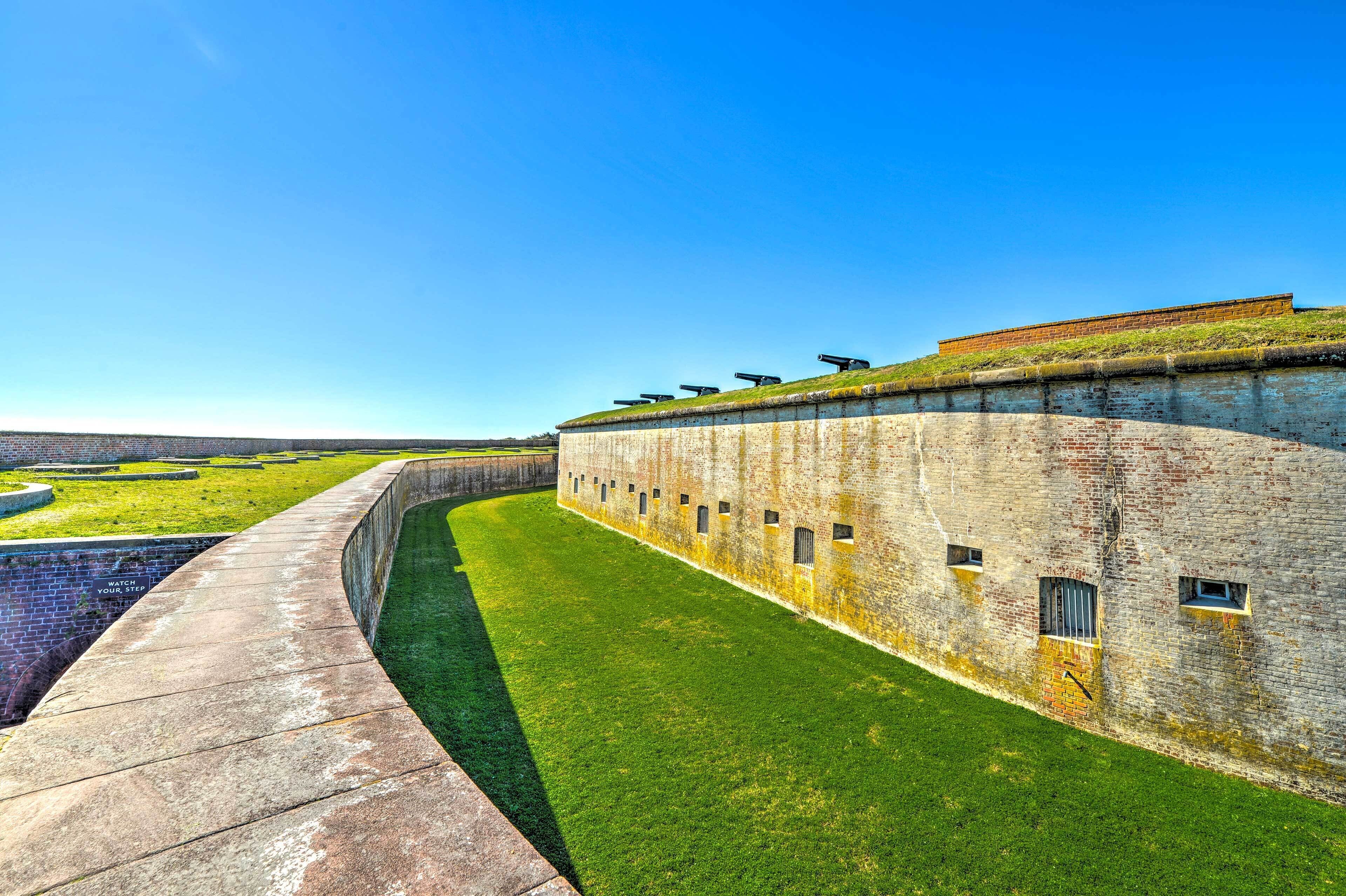 A long, curved brick wall with a grassy area in front, and a clear blue sky above.