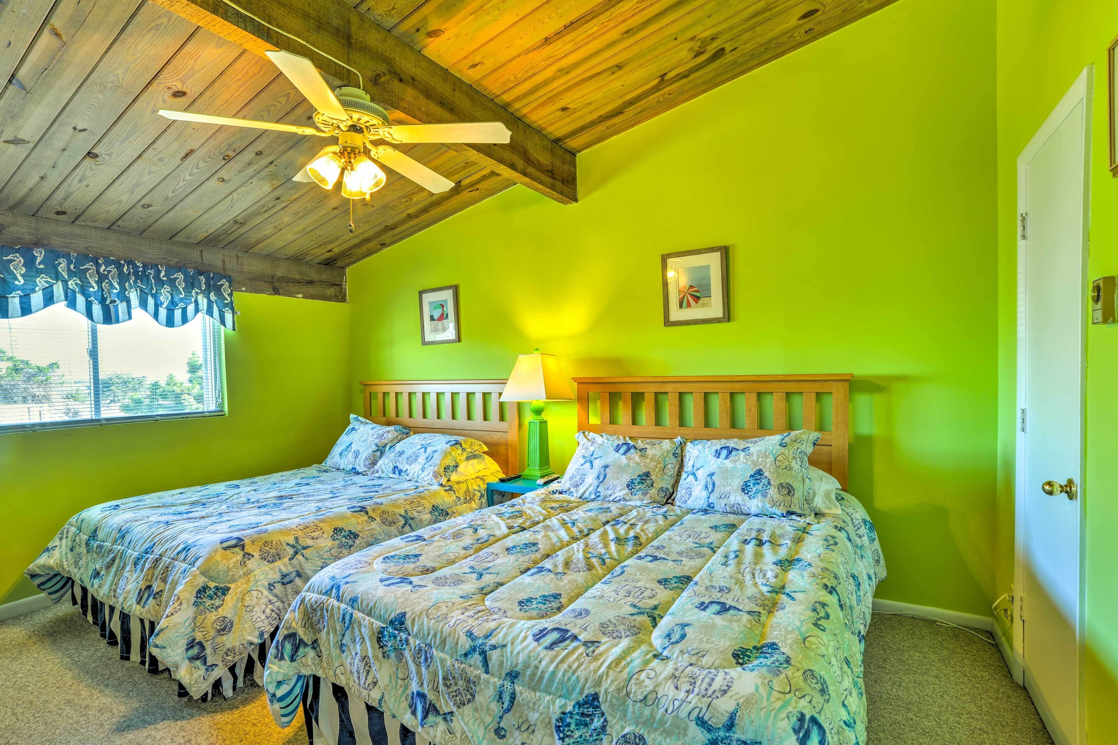A room with two beds, a ceiling fan, a window with curtains, and a door.