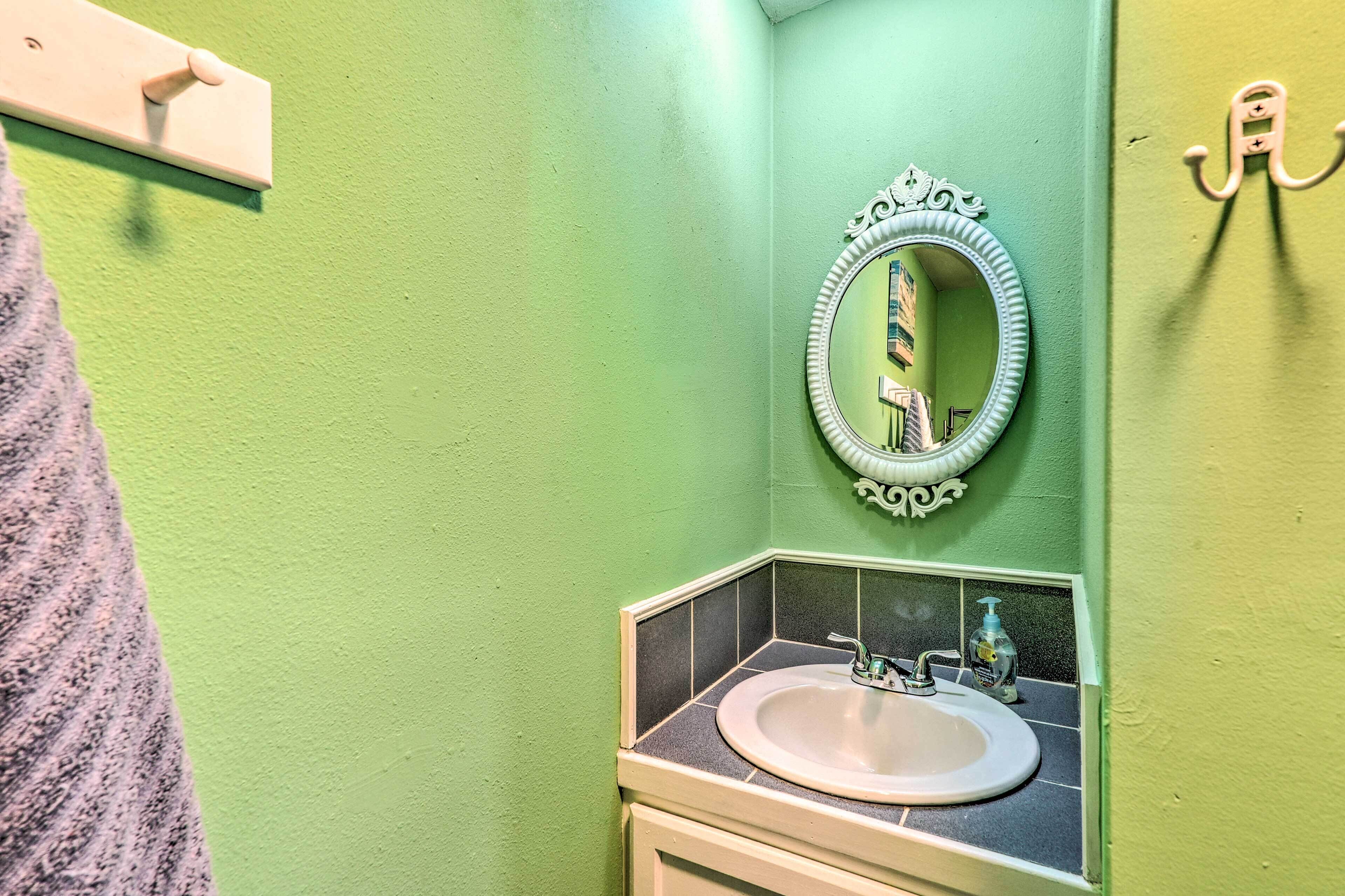 A bathroom with a green wall, a white sink with a mirror above it, and a towel hanging on the left.