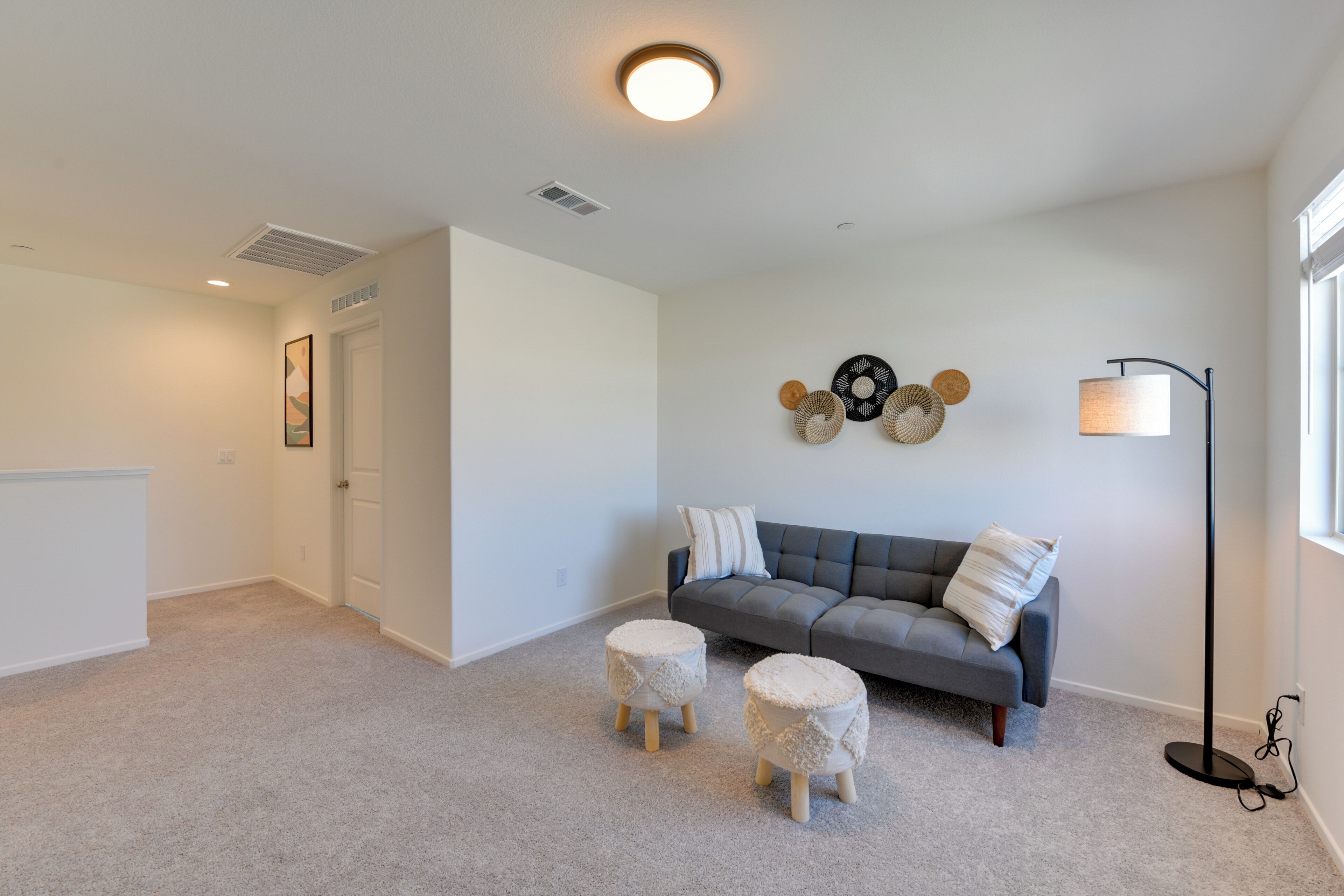 A living room with a grey sofa, two round ottomans, a floor lamp, and a wall decor piece.