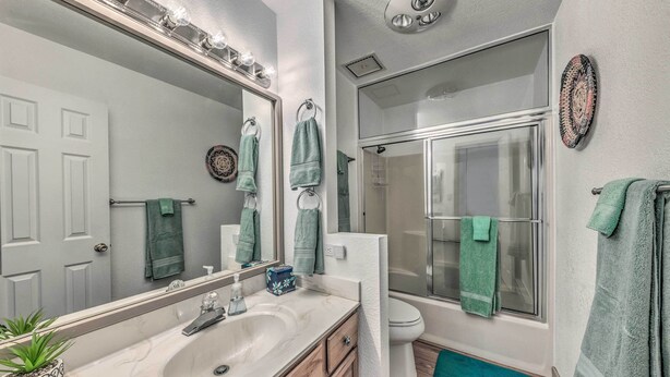 A bathroom with a sink, mirror, towel rack, toilet, and shower.