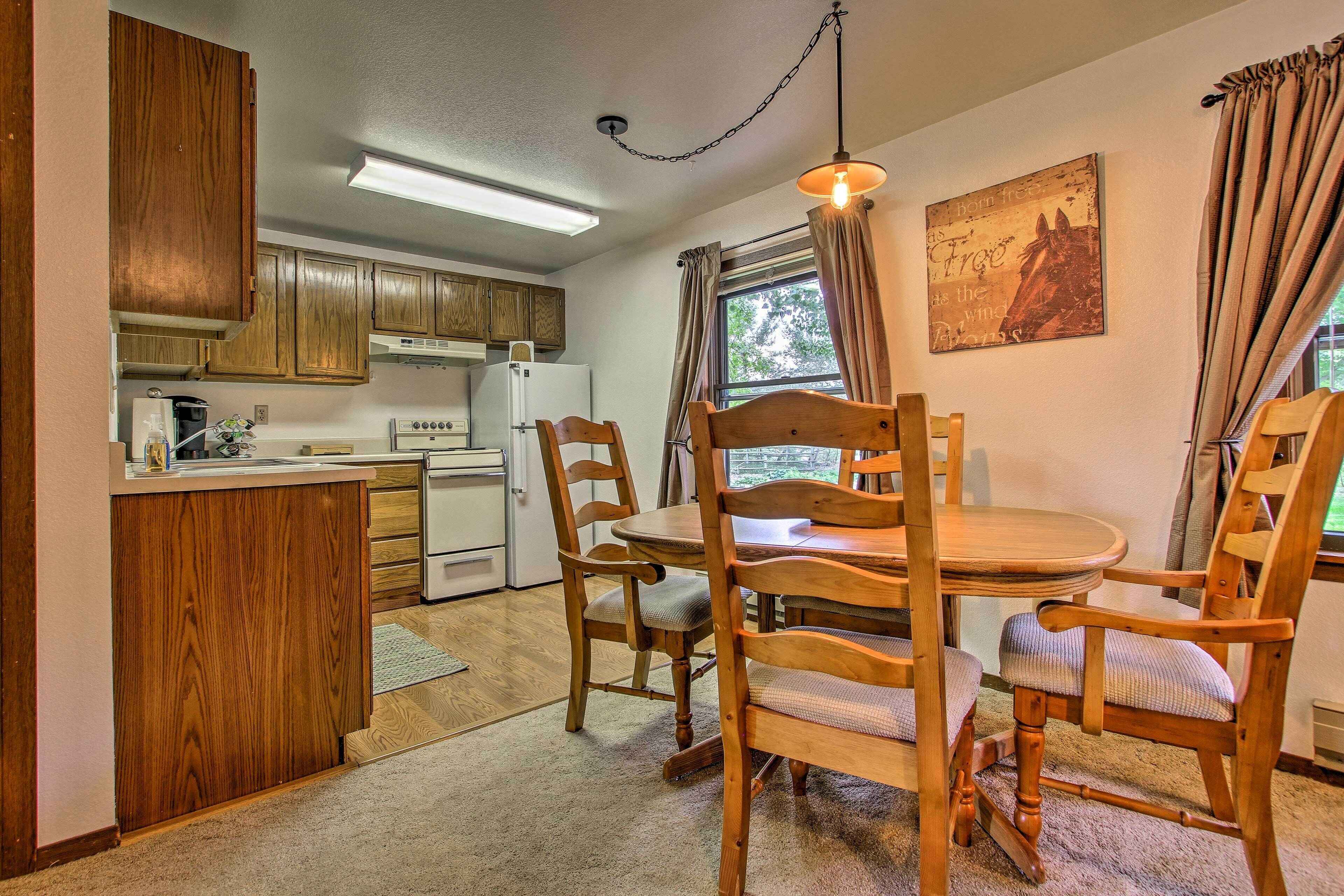 A kitchen with wooden cabinets, a dining table with chairs, a refrigerator, and a coffee maker.