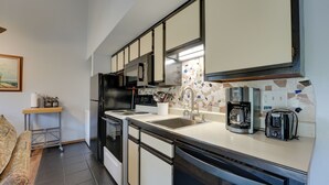 A compact kitchen with a microwave, stove, sink, and coffee maker.