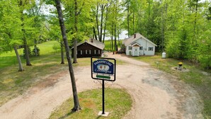 A sign for Paradise Lake Cottages with a gravel driveway leading to a wooden cabin and a white building. - Near Snowmobiling! Carp Lake Cottage w/ Fire Pit (Carp Lake)