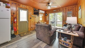 A cozy cabin interior with a wooden interior, a dining area, a living room with a couch and a table, and a refrigerator. - Near Snowmobiling! Carp Lake Cottage w/ Fire Pit (Carp Lake)