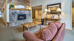 A living room with a stone fireplace, a wooden coffee table, a pink sofa, and a large mirror above a console table. - Copper Mountain Ski-in/ski-out Condo w/ Balcony! (Copper Mountain)