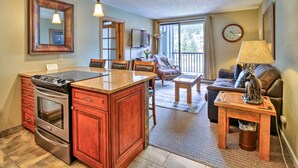 A kitchen with a stove, oven, and wooden cabinets, a dining area with chairs, a small table, and a couch. - Copper Mountain Ski-in/ski-out Condo w/ Balcony! (Copper Mountain)
