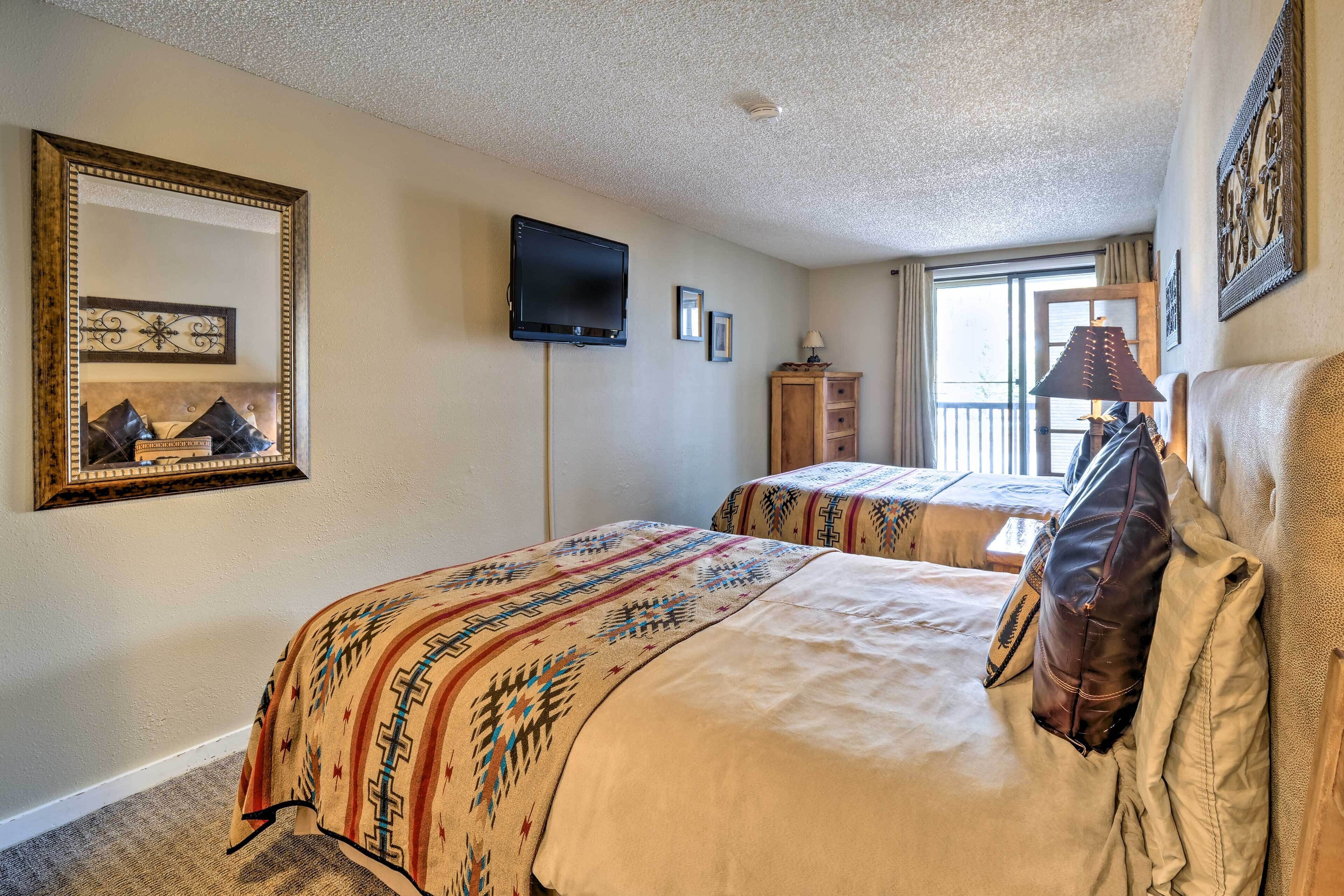A hotel room with two beds, a TV, a mirror, and a window with curtains.