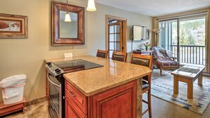 A kitchen with granite countertops, wooden cabinets, a built-in oven, and a dining area with a table and chairs. - Copper Mountain Ski-in/ski-out Condo w/ Balcony! (Copper Mountain)