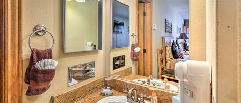 A bathroom with a granite countertop sink, a large mirror, a towel ring with a towel, a soap dispenser, and a handheld showerhead.