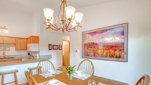 A dining area with a wooden table set for four, surrounded by chairs, a chandelier, and a painting of a landscape on the wall. - Condo w/ Mtn View < 1 Mi to Steamboat Resort! (Steamboat Springs)
