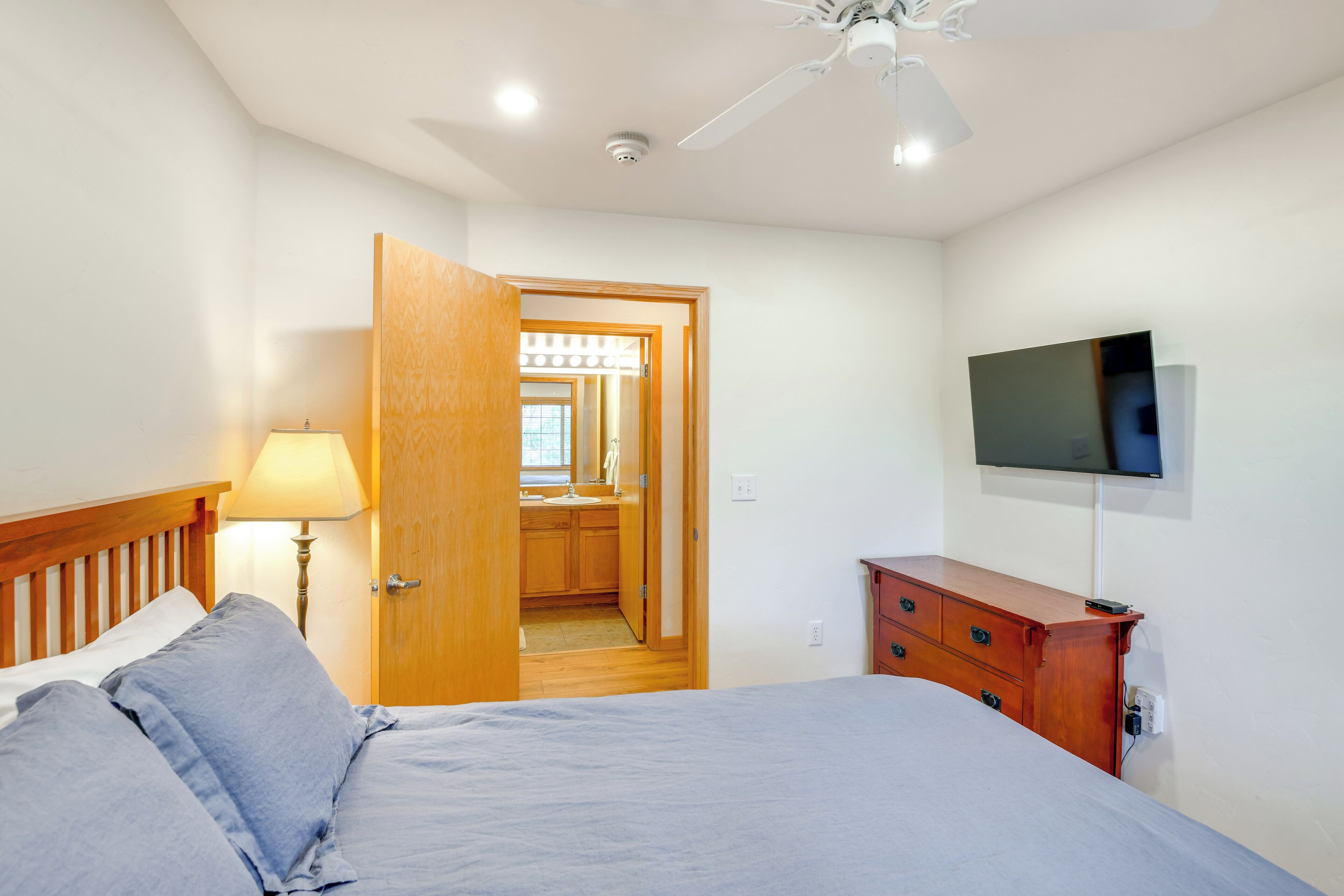 Ein Schlafzimmer mit einem Bett, einer Holzkommode, einem an der Wand montierten Fernseher und einem Deckenventilator.