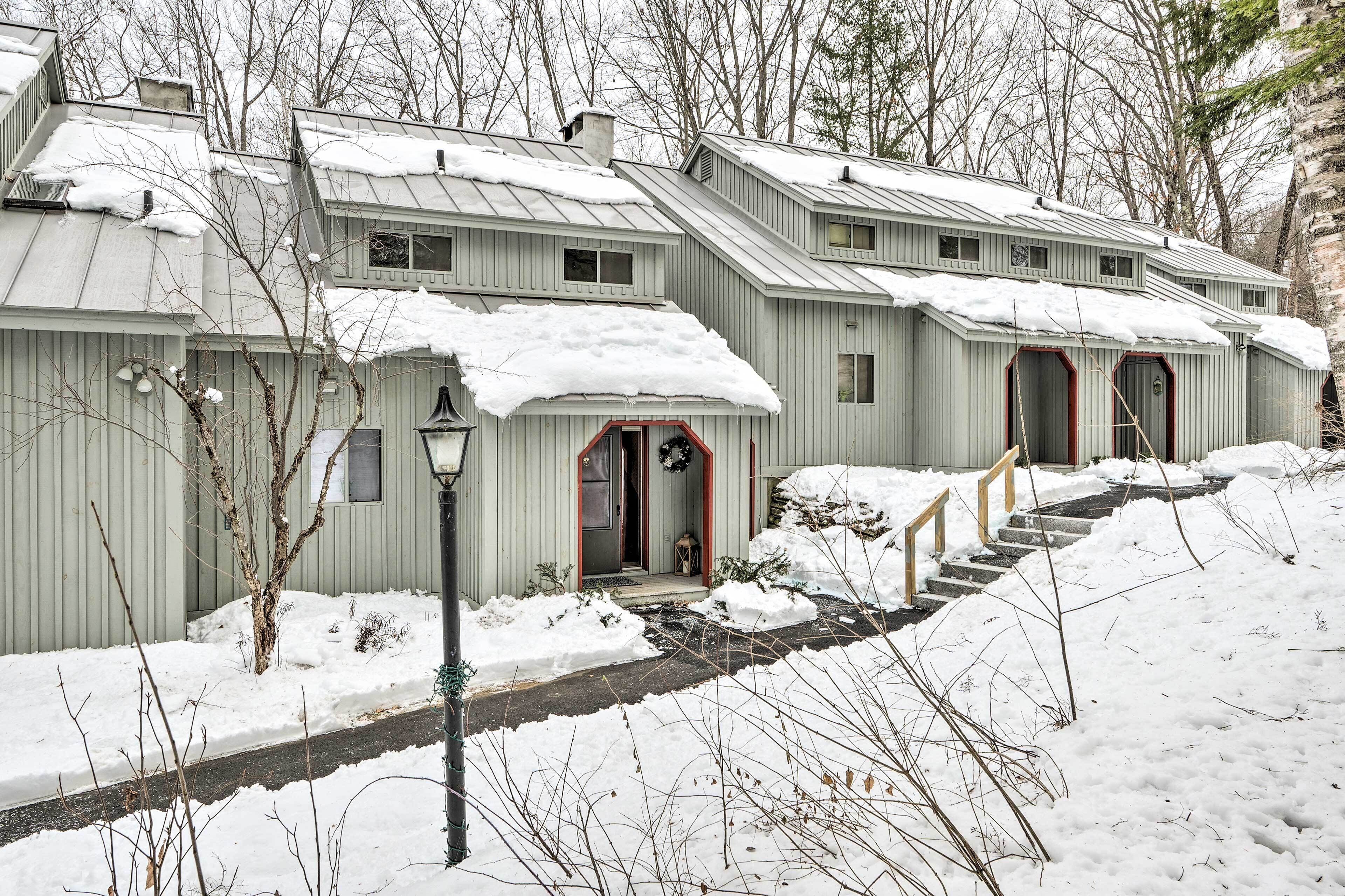 Une rangée de cabanes rustiques aux toits métalliques, aux portes en bois, et un paysage recouvert de neige.