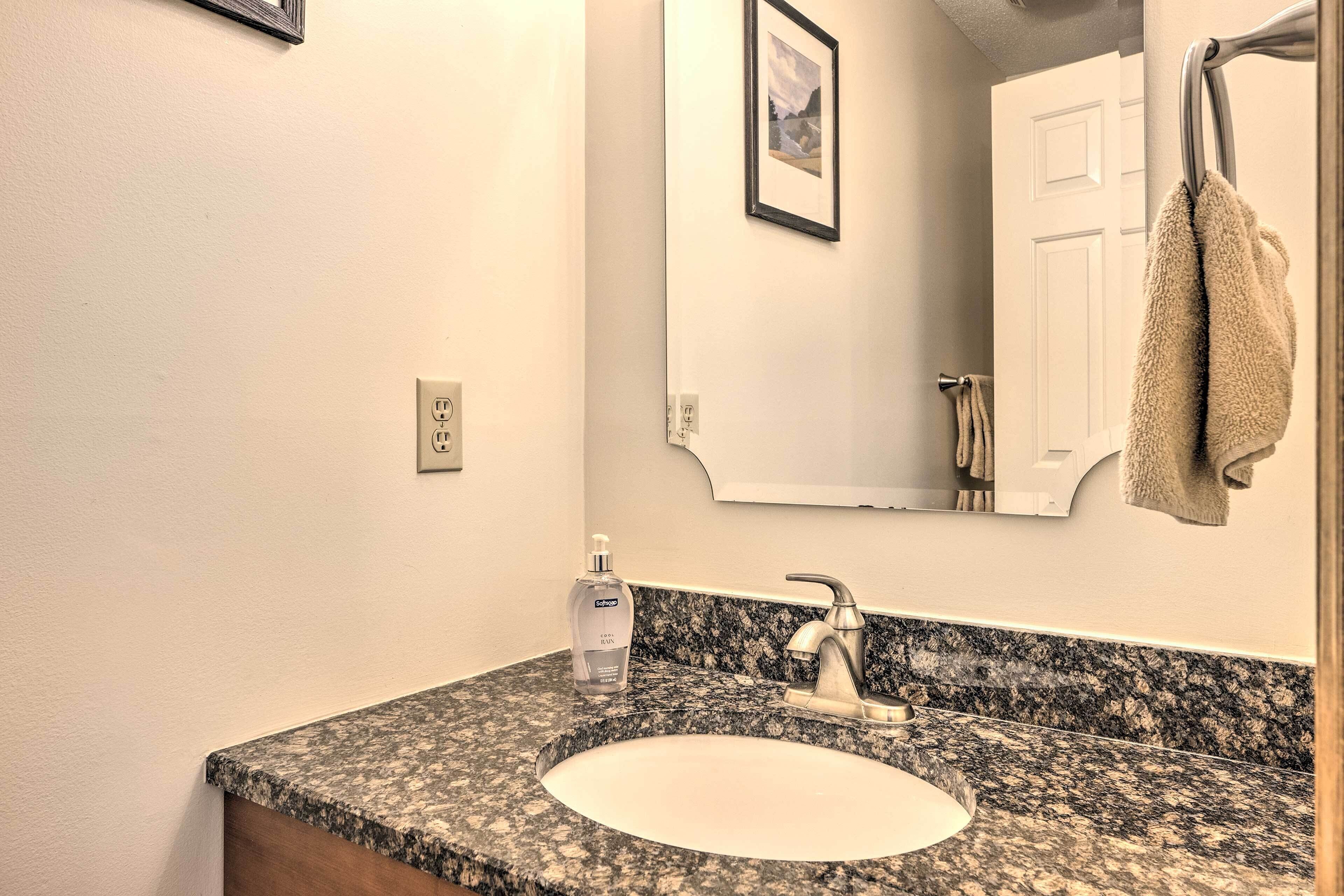 A bathroom with a granite countertop, a white sink, a faucet, a mirror, and a towel hanging on a towel rack.