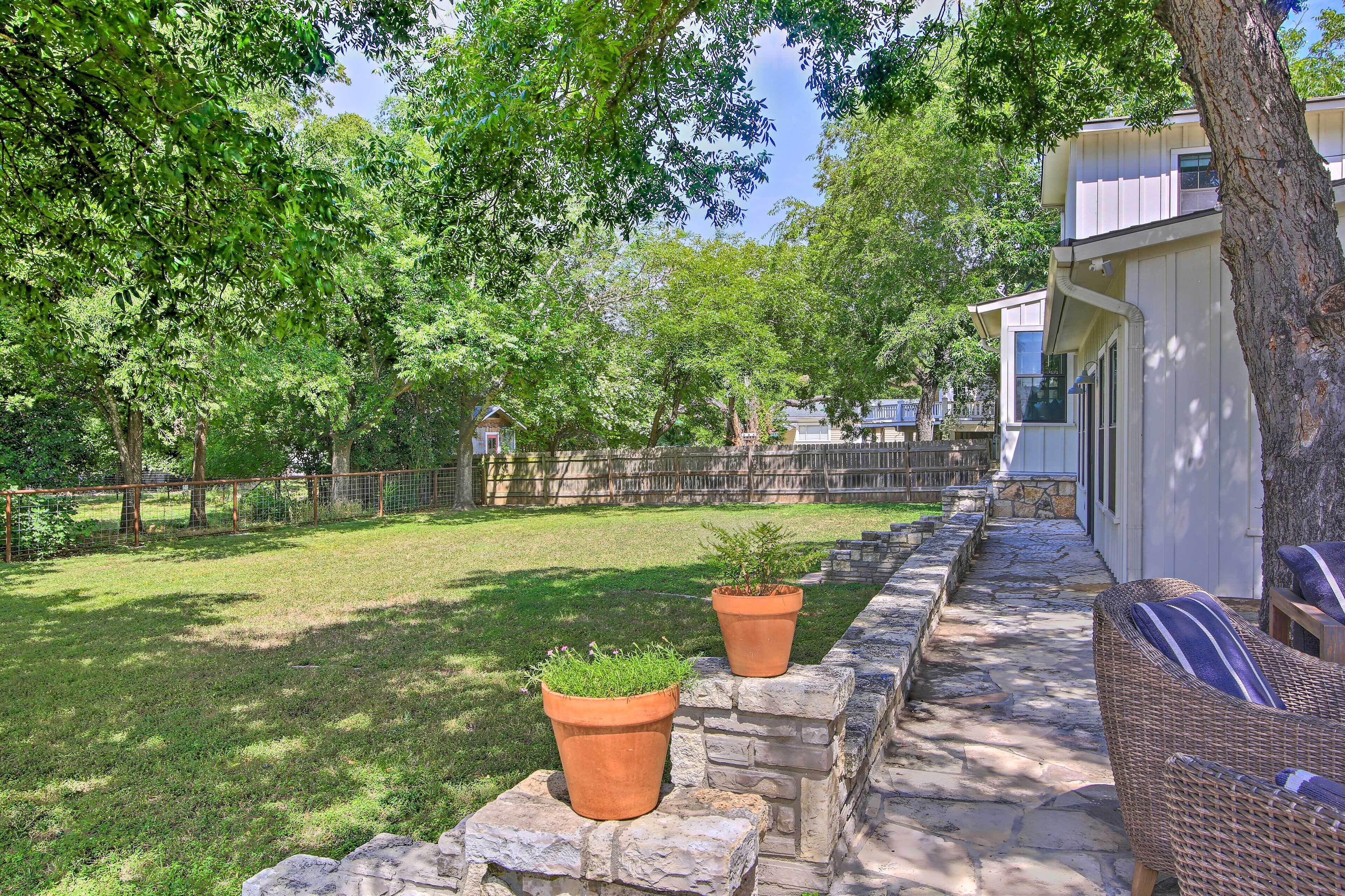 A patio area with stone steps, two potted plants, wicker furniture, and a view of a house with a tree in the background.