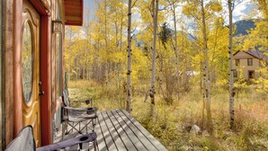 A wooden deck with a bench and a chair, overlooking a forest with yellow foliage and a mountain in the background. - Colorful Cabin w/ Teepee, Fire Pits & Mtn Views! (Carbondale)