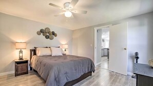 Een slaapkamer met een bed, twee bedlampjes, een plafondventilator en een deur naar een andere kamer.