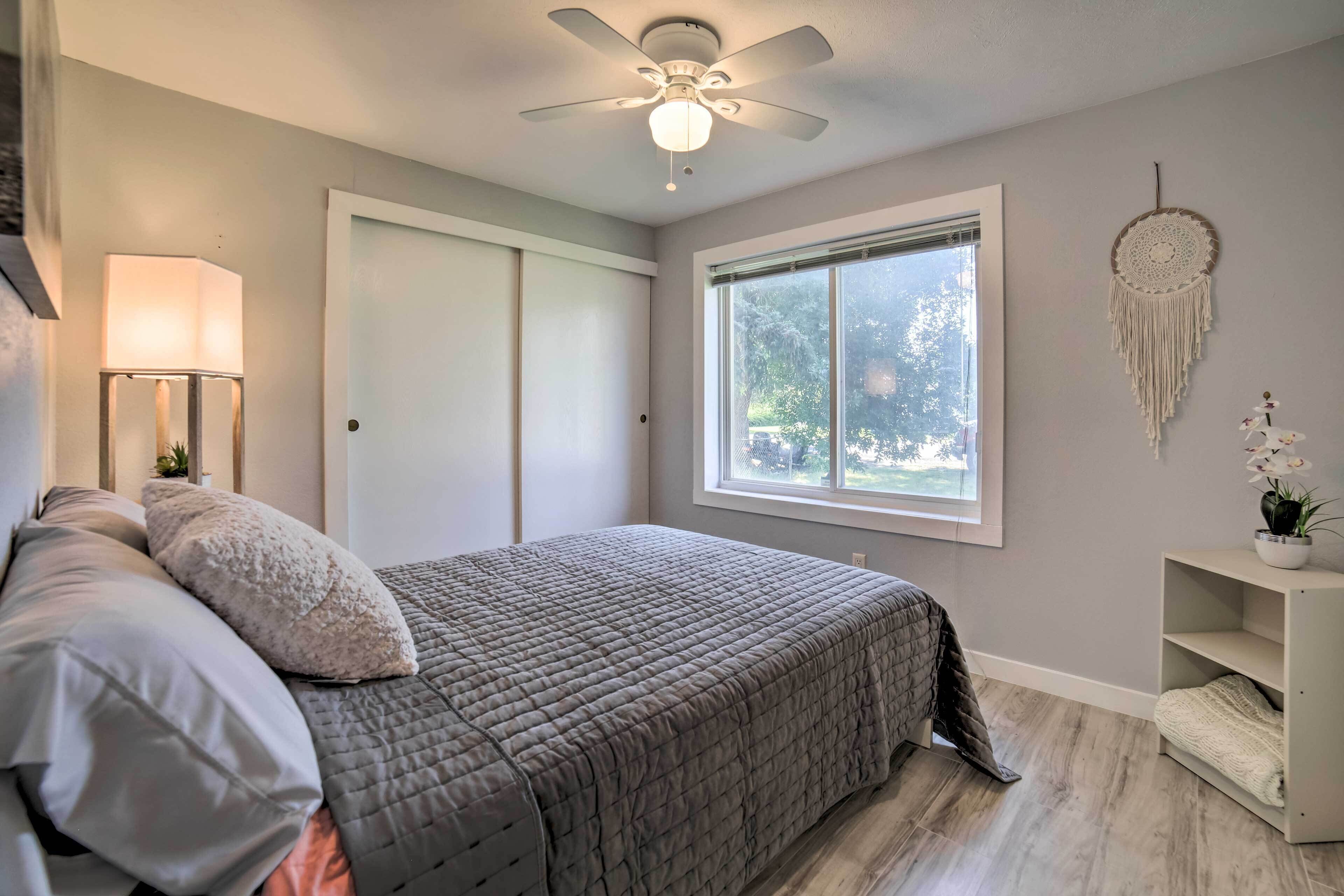A bedroom with a bed, a ceiling fan, a window, a nightstand, and a wall-mounted dreamcatcher.