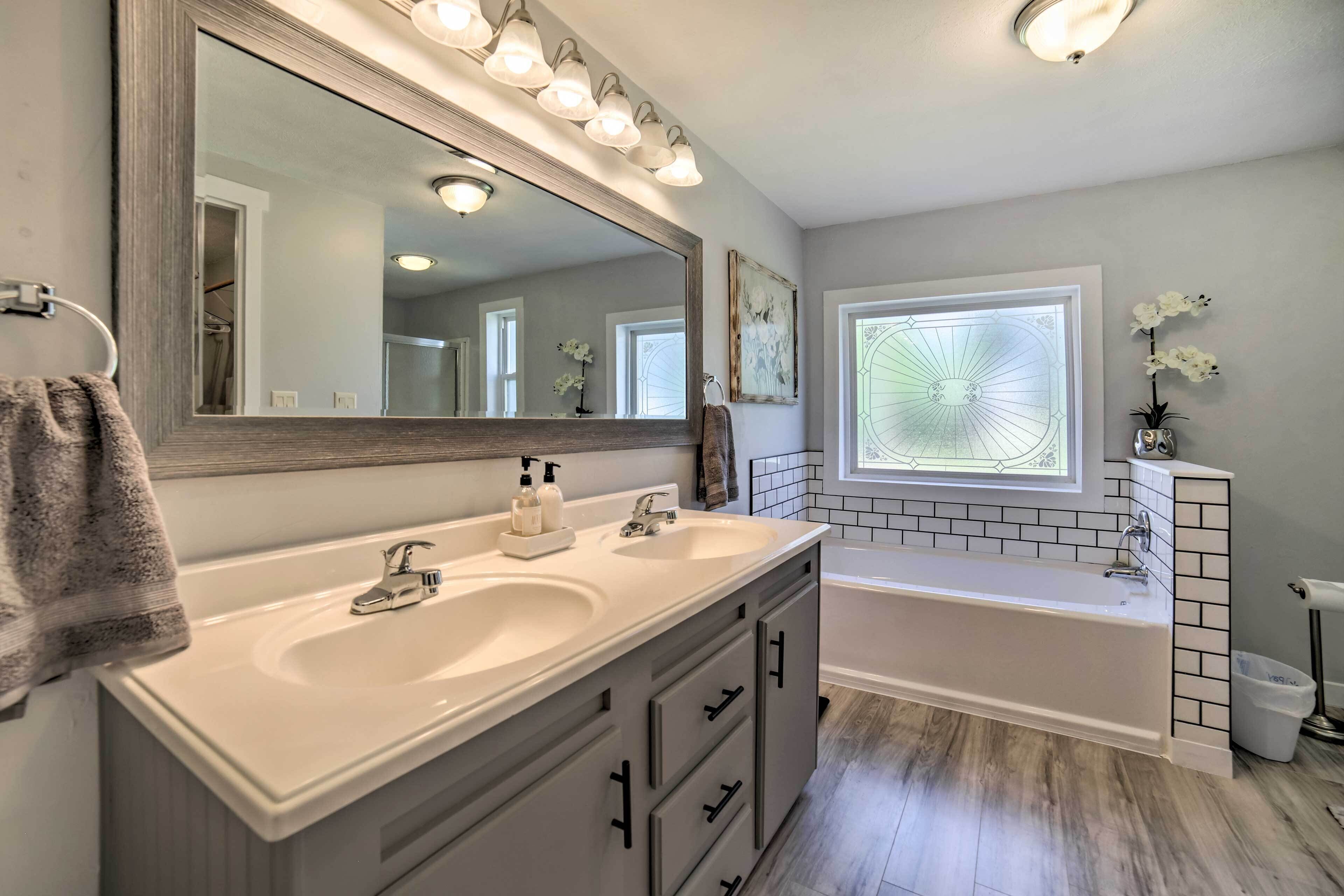 A bathroom with a large mirror, two sinks, a bathtub, and a window with a view of the sky.