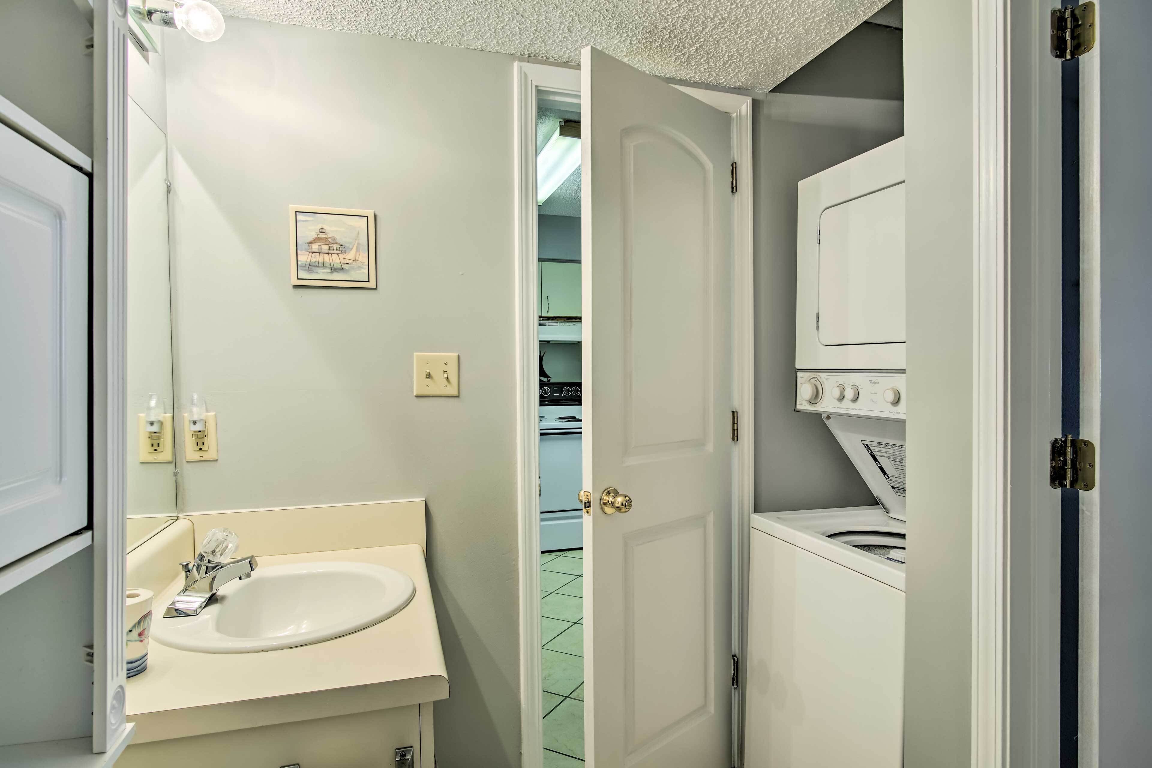 A bathroom with a sink, mirror, and a door leading to a laundry area with a washing machine.