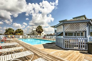 A wooden deck with a pool, lounge chairs, and a covered area with a lattice design. - Gulf Shores Condo w/ Pool Access: Steps to Beach! (Gulf Shores)